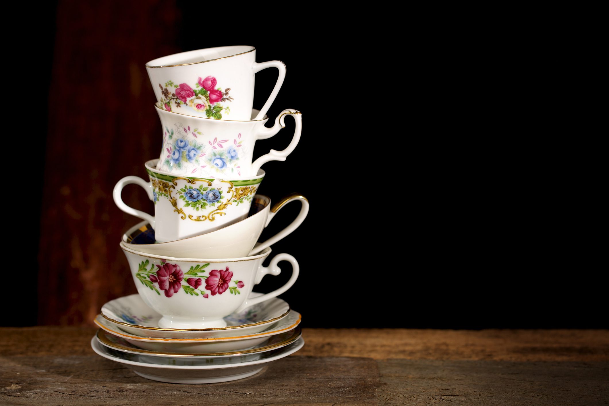 Various vintage porcelain teacups with floral decoration on dark background.