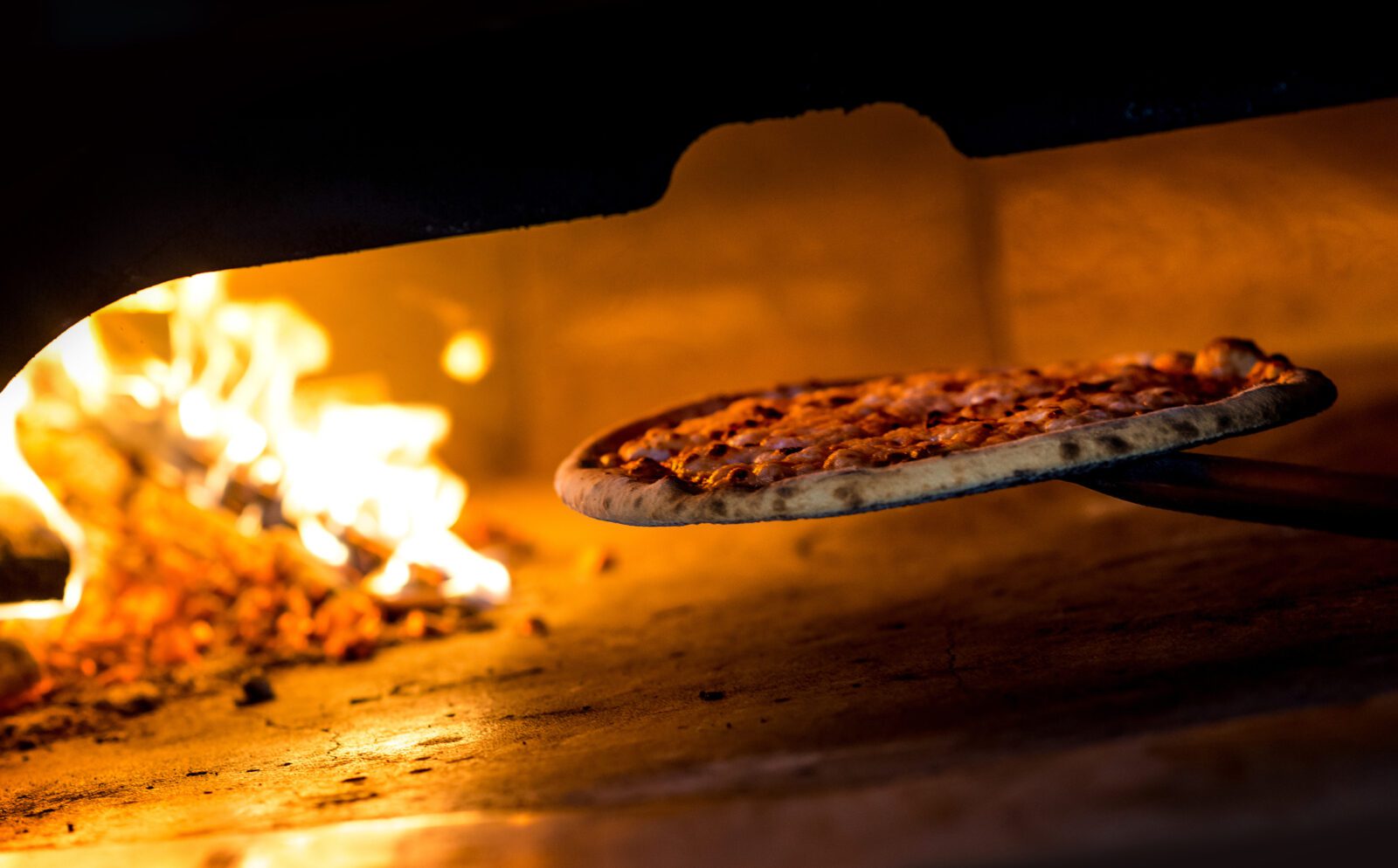 A pizza is removed from a wood burning oven in a classic Italian restaurant