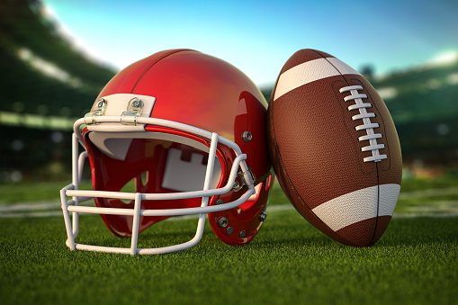 American football ball and helmet on the grass of football arena or stadium.